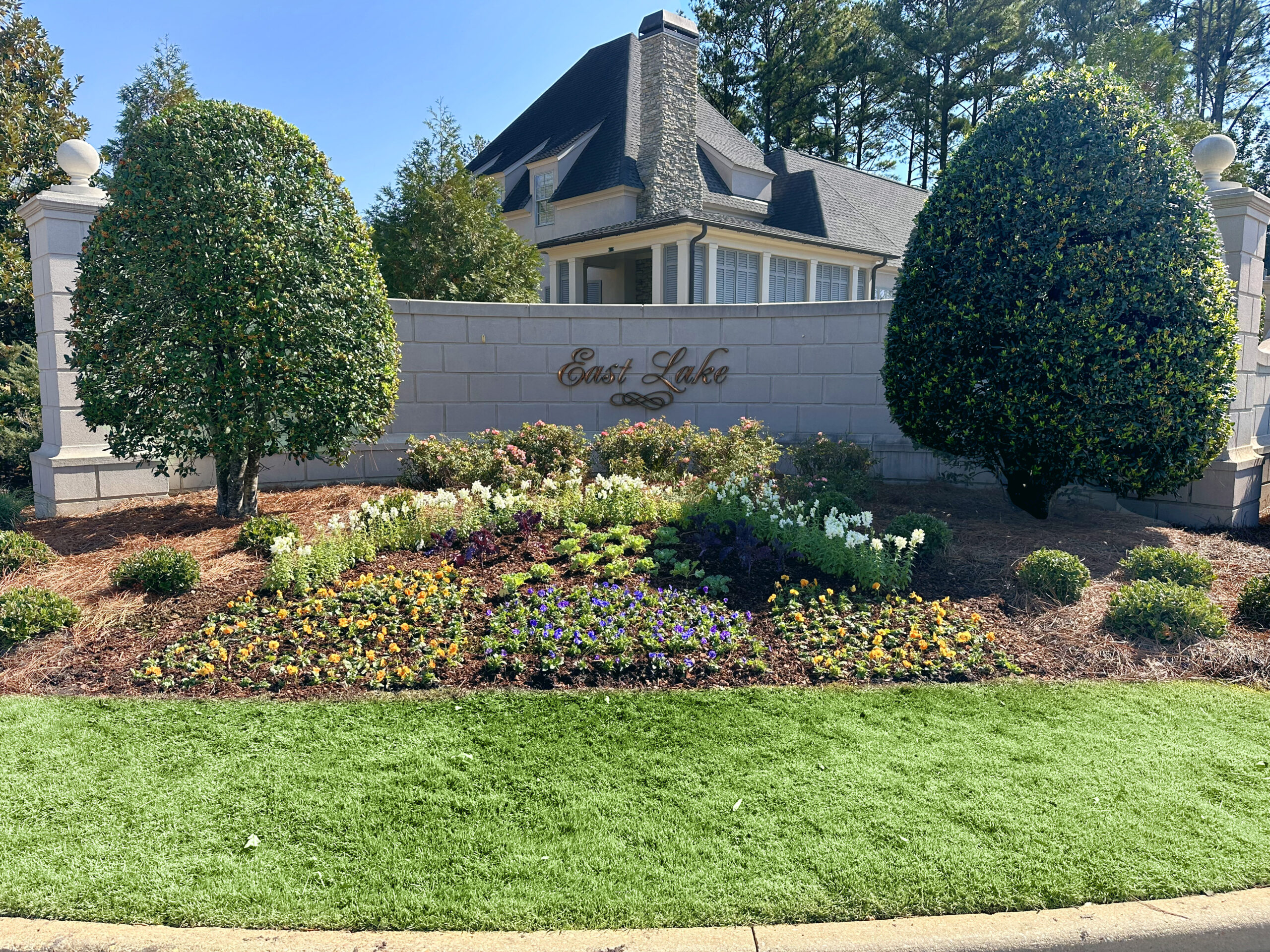 East lake neighborhood entrance ornamental garden bed multicolor flowers easter lillies pansies pruned shrub trees and english roses