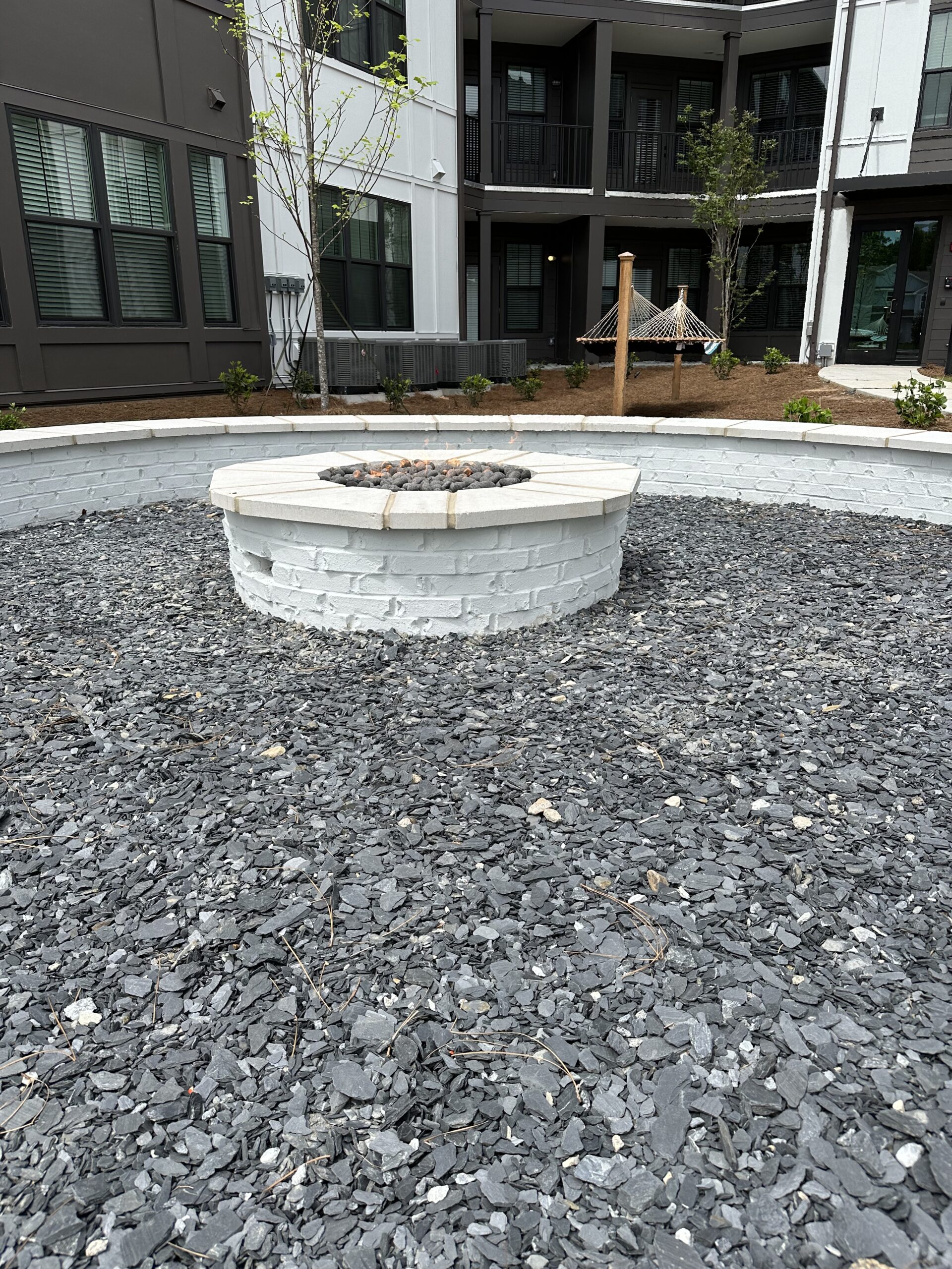 stone work brick fire pit at apartment complex surrounded by gravel and brick seating 