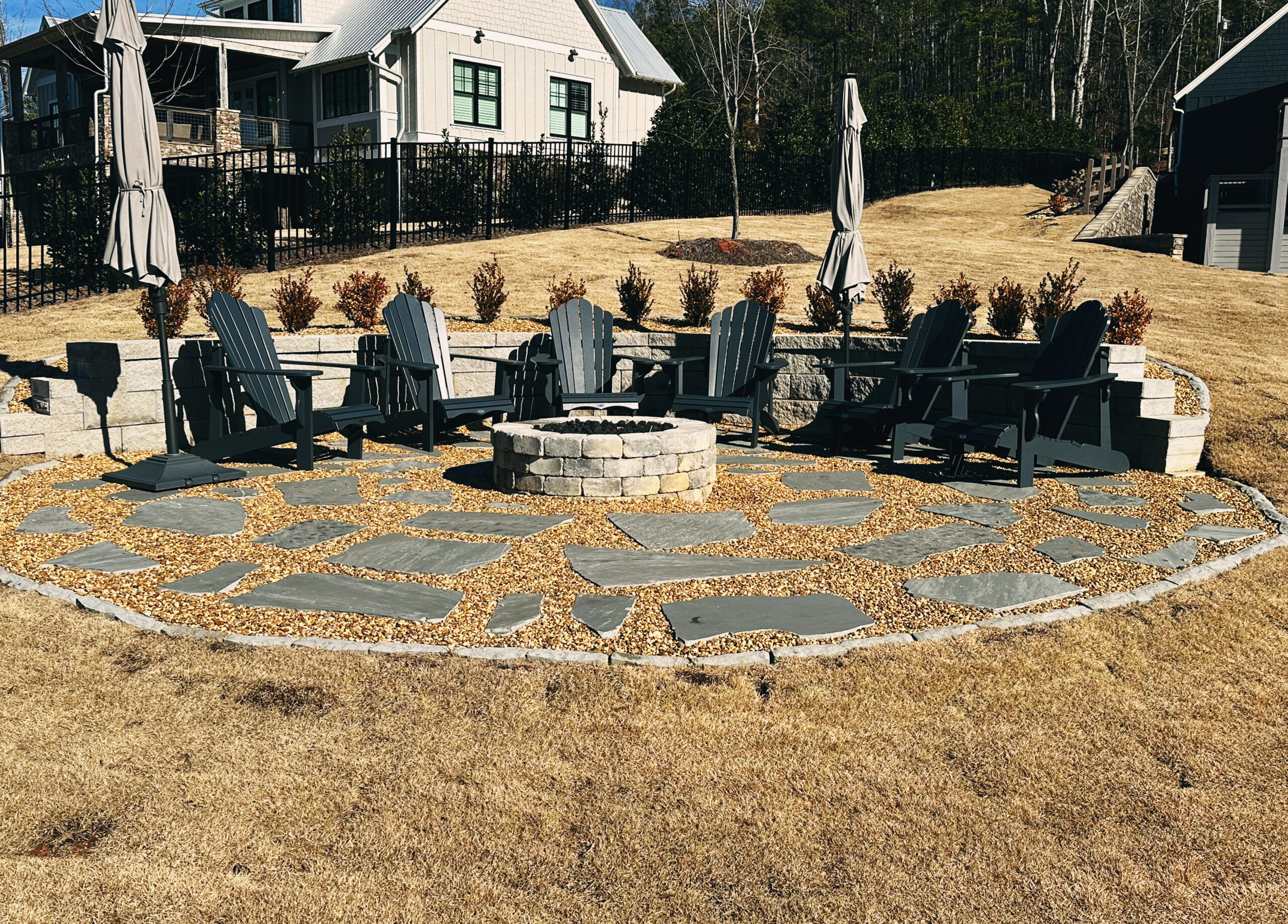 stone fire pit with a circle of adirondack chairs around it and a retaining wall and flagstone slabs in residential yard